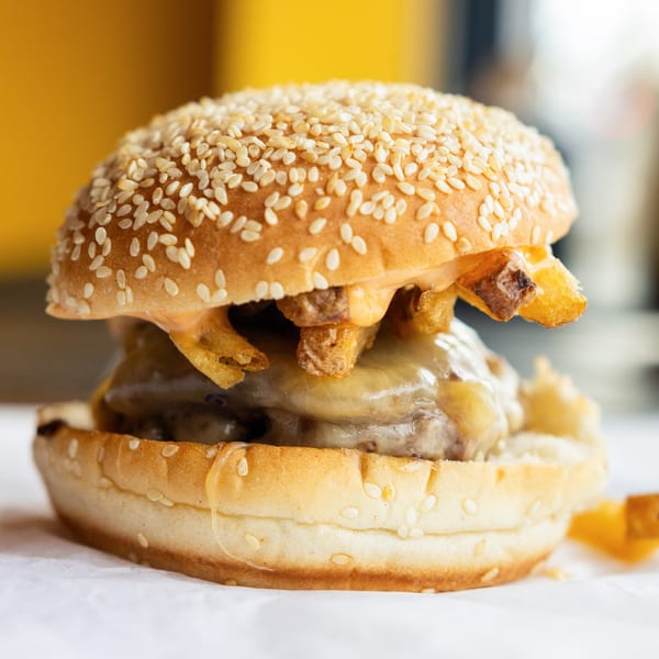 A GoldBurgers burger with melted cheese, special sauce, and fries on a sesame seed bun.