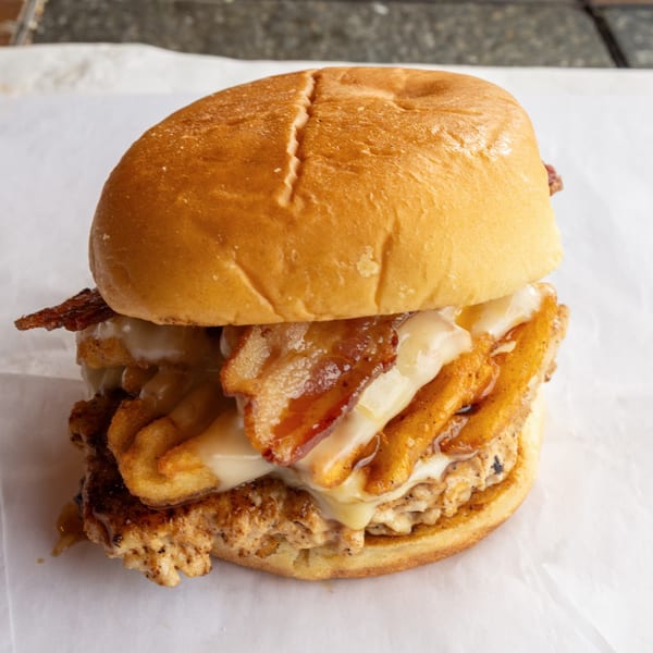 A GoldBurgers burger with bacon, fries, and melted cheese on a bun.