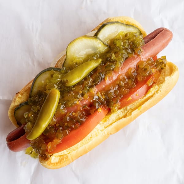 GoldBurgers hot dog with relish, pickles, and tomatoes on a white paper background.