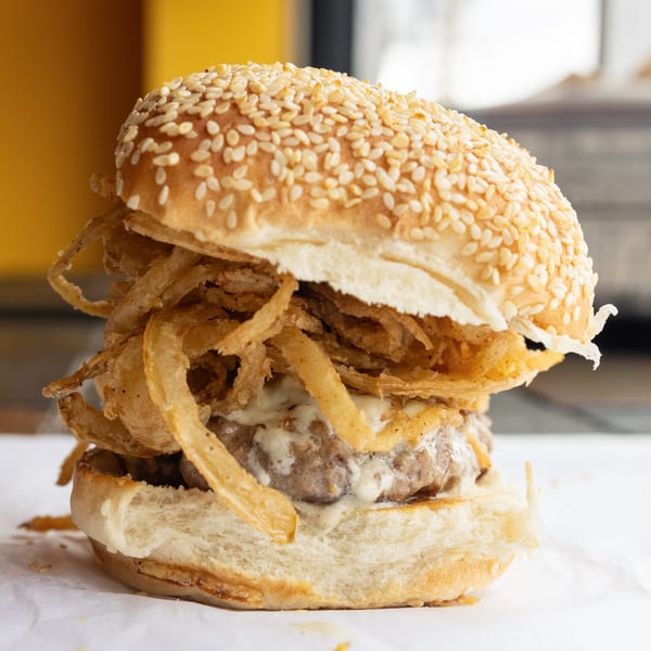 A GoldBurgers burger with a sesame seed bun, crispy fried onions, and creamy sauce.