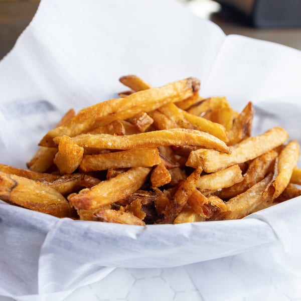 Close-up of a basket of GoldBurgers' golden-brown, crispy french fries, lightly salted.