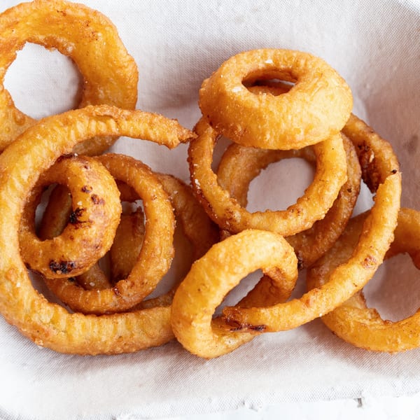 Close-up of crispy, golden-brown onion rings, some curly, in a white paper-lined basket.