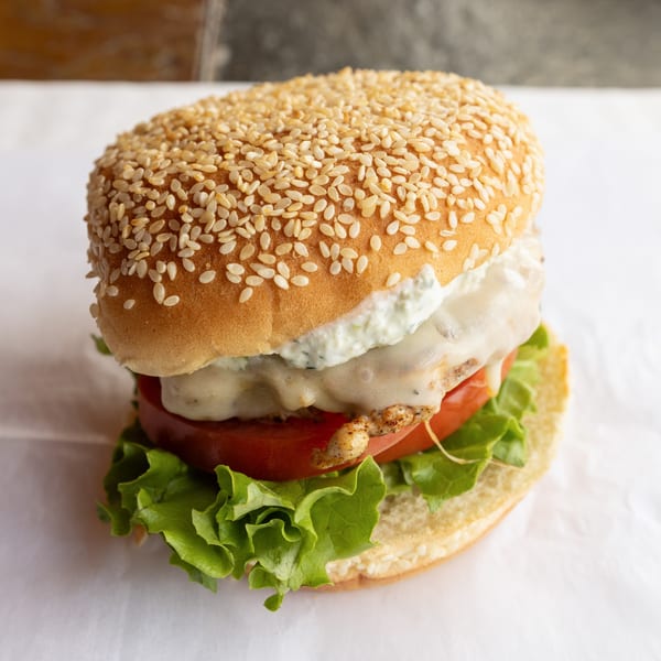 A GoldBurgers chicken burger with melted cheese, tzatziki, tomato, and lettuce on a sesame bun.
