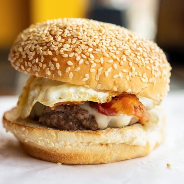 A GoldBurgers burger with a beef patty, melted cheese, bacon, and a fried egg on a sesame seed bun.
